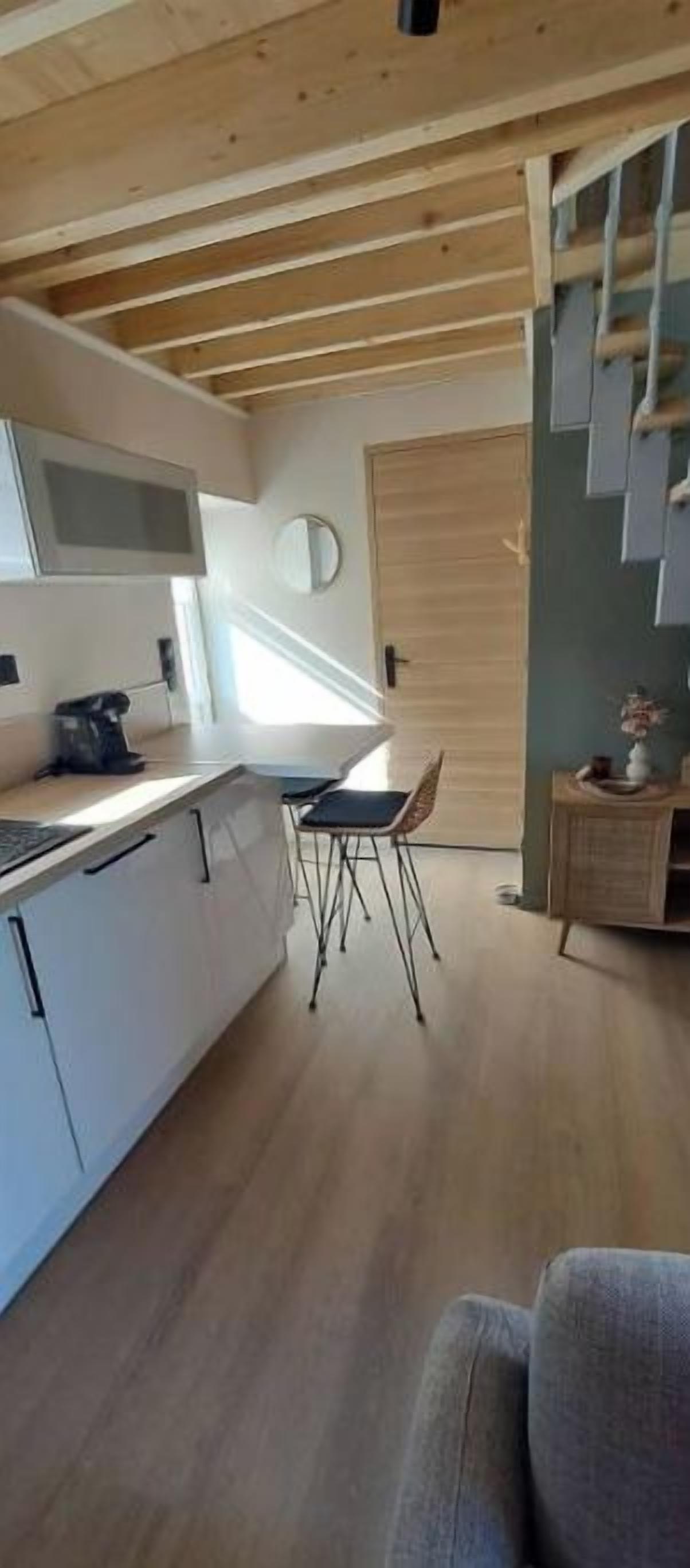 Et køkken med hvide skabe, trælofter, et spiseområde med en stol og et lille bord.