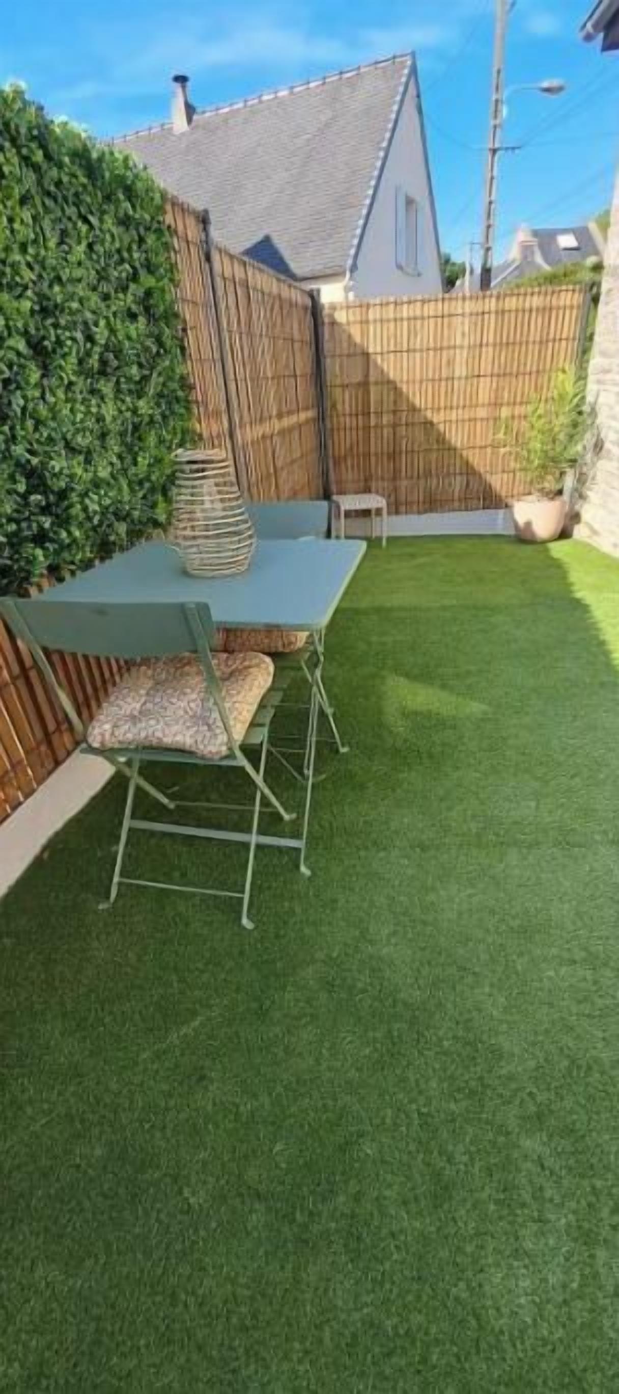 Un patio trasero con mesa y sillas, un cerco de madera y un seto.