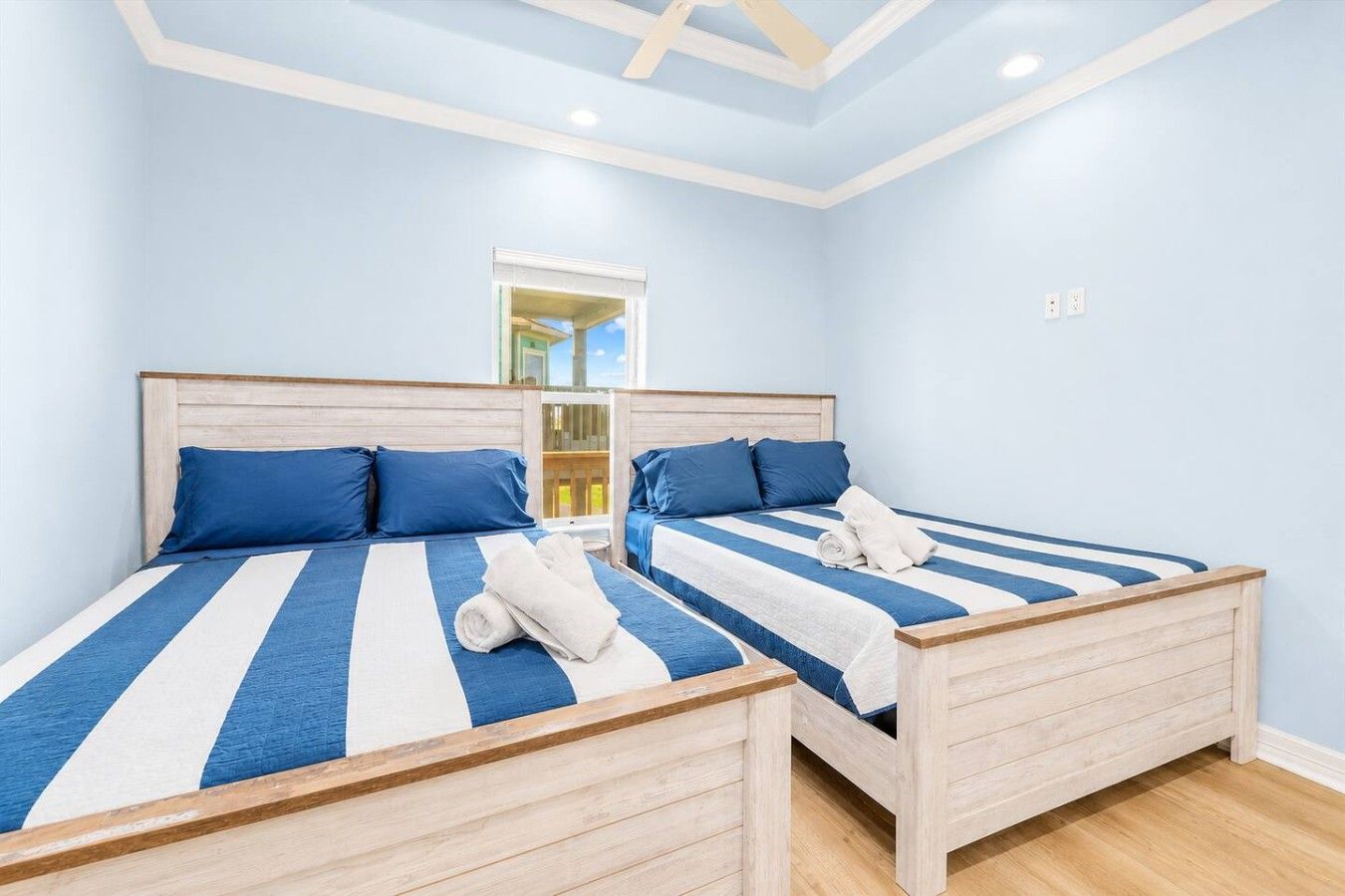 Ein Doppelbett mit blau-weißer Streifenwäsche, Holz-Kopfteilen und einem kleinen Fenster.