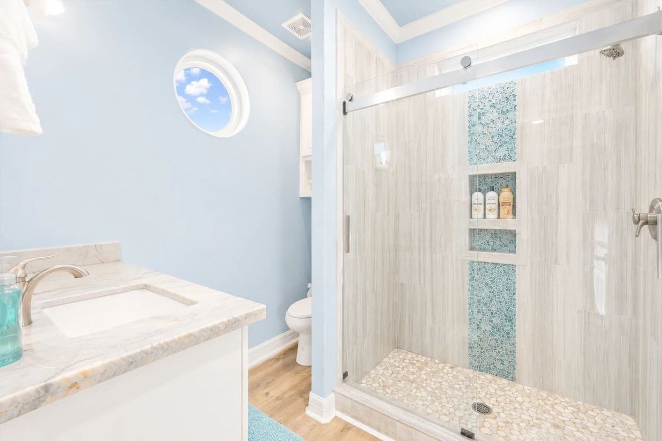 Un baño con lavamanos de mármol, cabina de ducha con mampara de vidrio y un tragaluz circular.