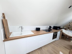 A modern kitchen with a wooden countertop, white cabinets, a built-in oven, and a dining area with a wicker chair. - Cocon Pierre & Lumière, Cœur de Saint-Patern, Vannes (Vannes)