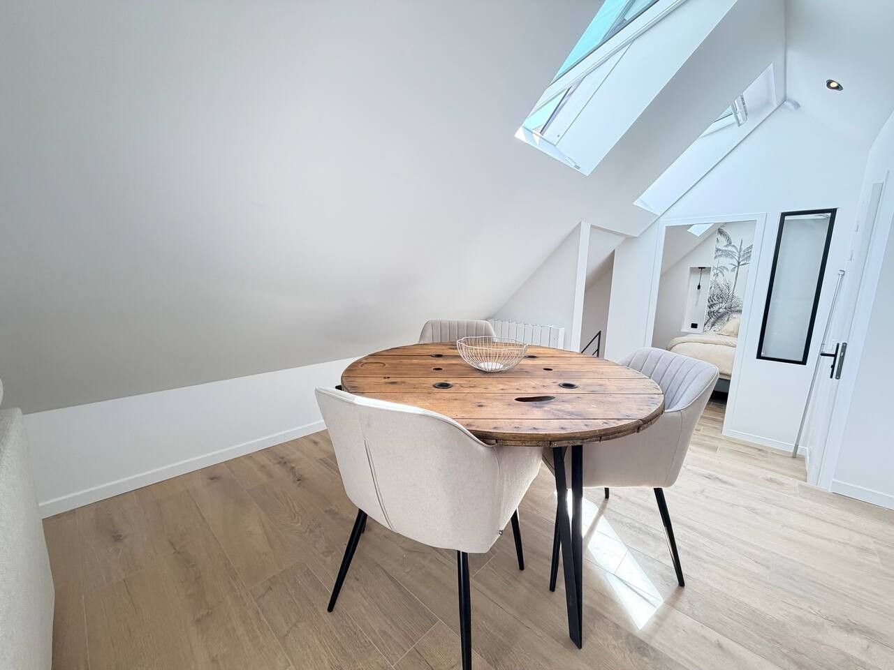 Et moderne spiseområde med et rundt træbord, to stole og et ovenlys.