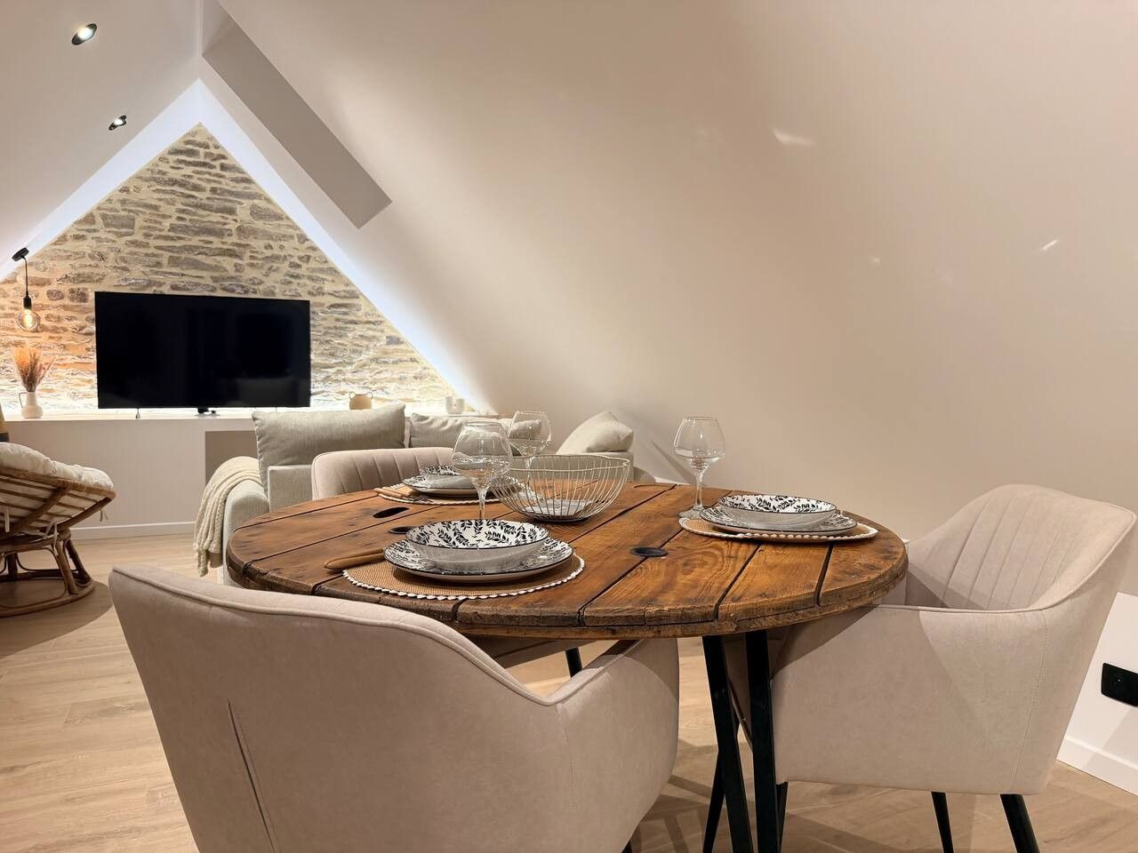 Un espace repas avec une table ronde en bois, des chaises blanches et un mur en pierre en arrière-plan.