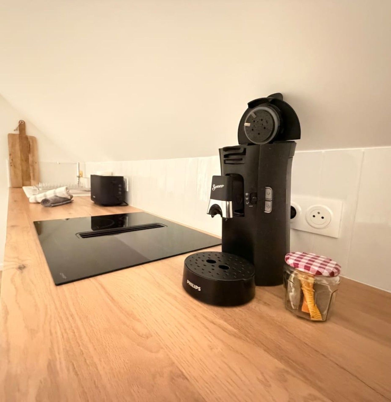A kitchen with a coffee maker, a kettle, and a small container on a wooden countertop.