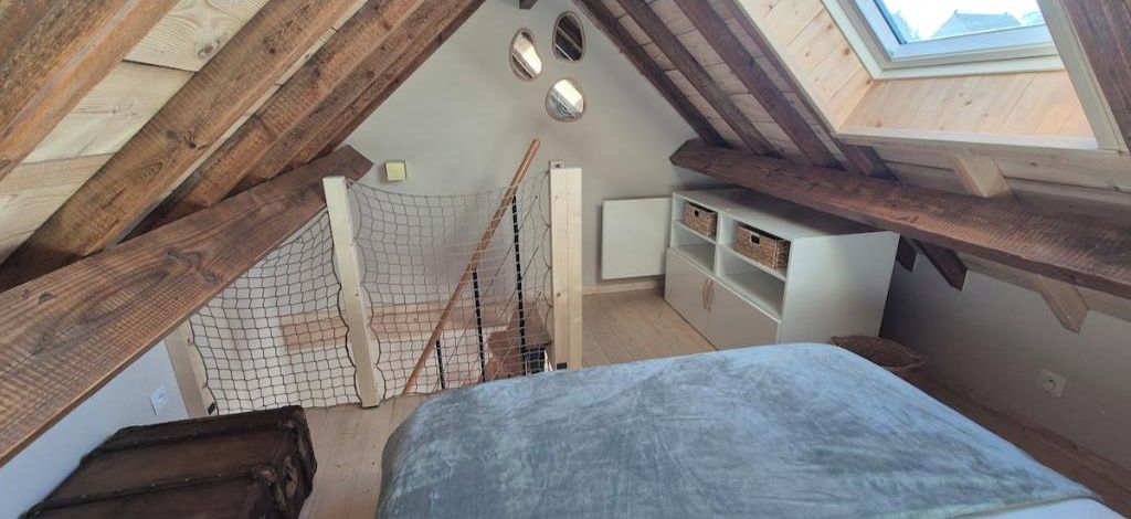 Techo inclinado con vigas de madera, una cama litera, un área de juegos con mosquitero y un tragaluz.
