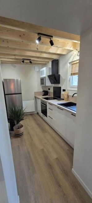 A modern kitchen with white cabinets, a stainless steel refrigerator, and a wooden ceiling. - A cozy home, perfect for exploring the Cotentin region (Normandie)