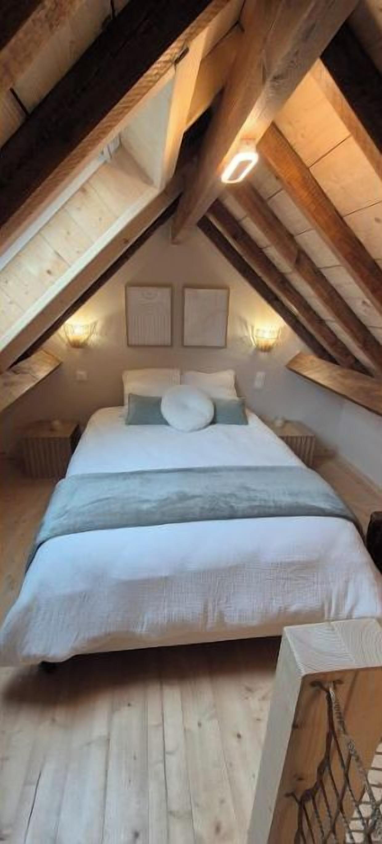Une chambre avec un grand lit, des poutres apparentes et deux lampes fixées au mur.