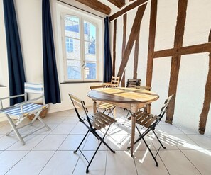 Un comedor con una mesa redonda de madera y cuatro sillas, una ventana con cortinas y vigas de madera a la vista en el techo.