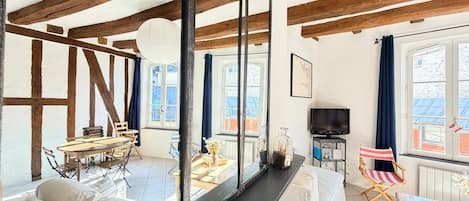 A spacious living area with a high ceiling, wooden beams, a large mirror, a sofa, a dining table, and a television.