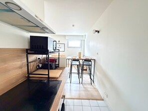 A compact kitchen with a black countertop, a wooden shelf unit, and a dining area with two chairs and a table. - Modern studio apartment in Vannes, just a stone's throw from the city walls (Vannes)