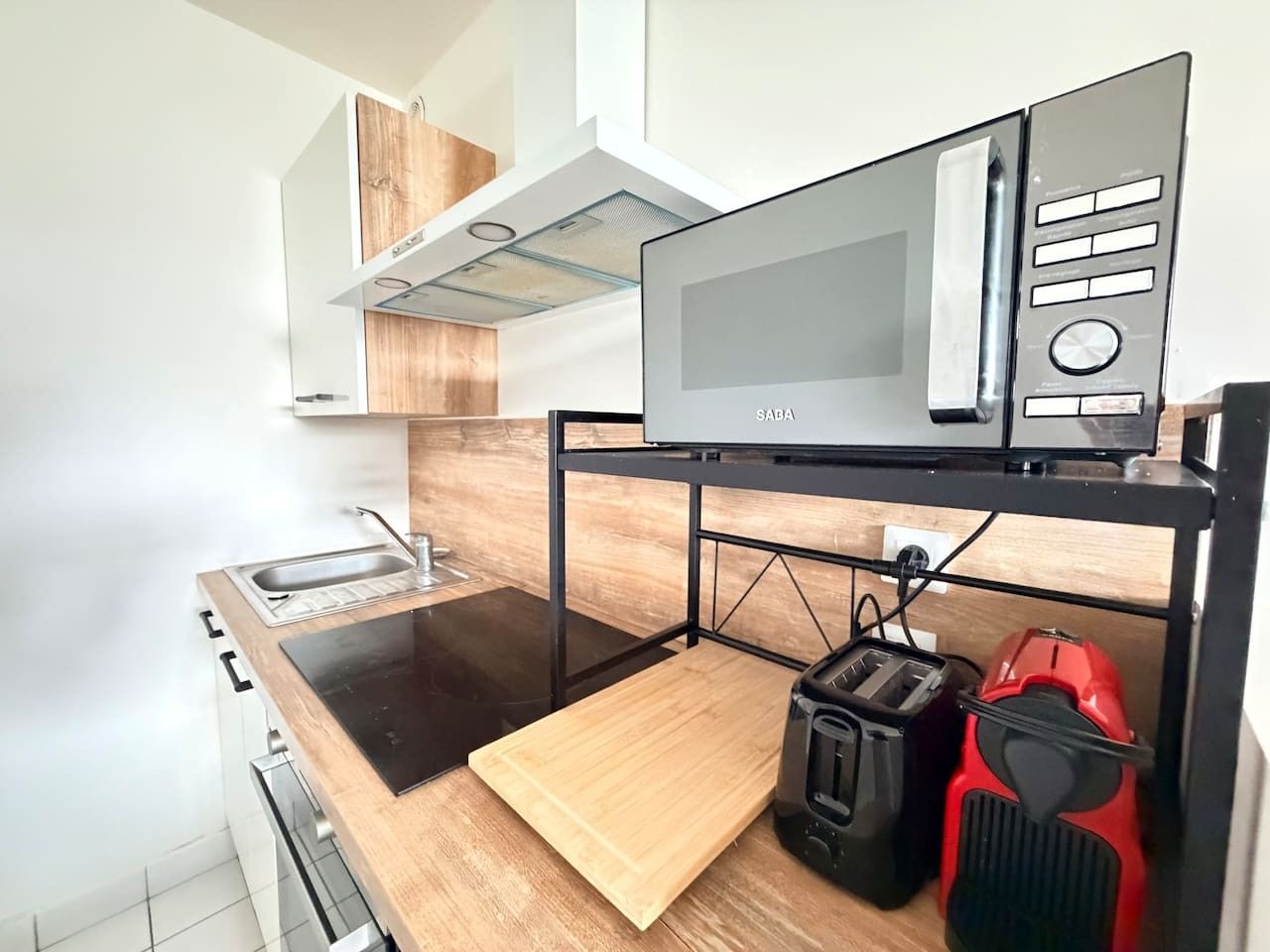 A compact kitchen with a microwave, toaster, and a red appliance on a shelf.