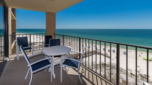 A balcony with a table and chairs, overlooking a beach with a clear view of the ocean. - Phoenix I 1077 2 Bedroom Condo (Orange Beach)