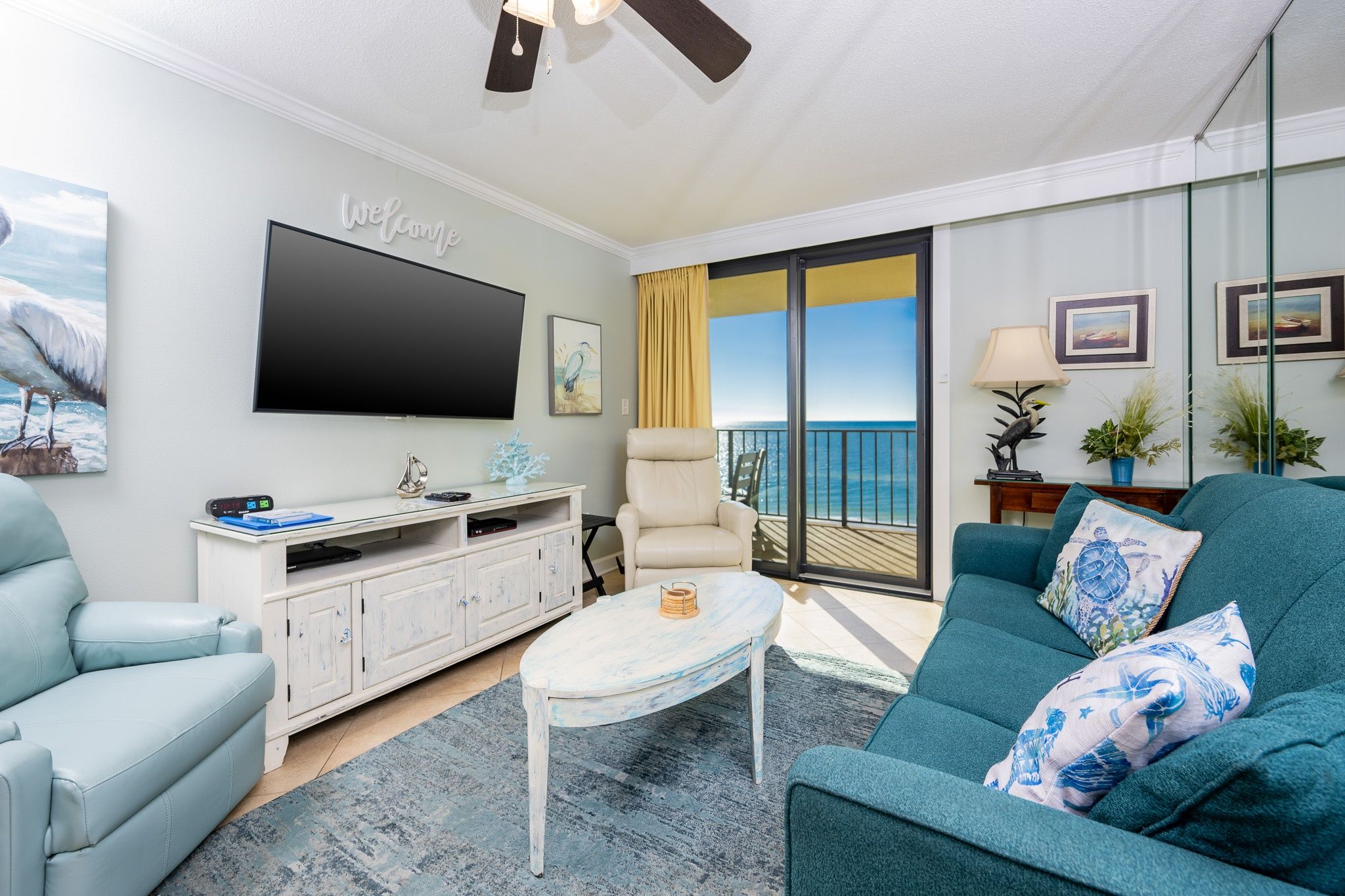 A living room with a television, a sofa, a chair, a coffee table, and a balcony with a view.