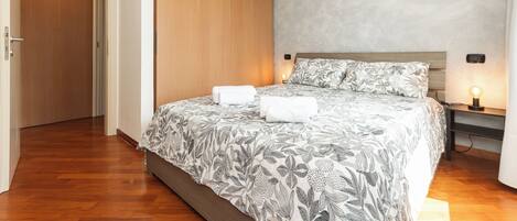 A bedroom with a bed, a nightstand, a wall-mounted lamp, and a door.