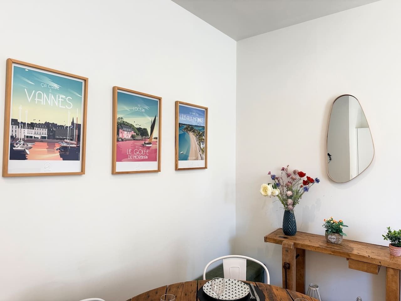 Een kamer met een eettafel, een spiegel en drie ingelijste foto's aan de muur.