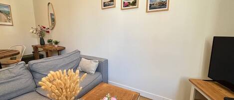 Una sala de estar con un sofá gris, una mesa de centro de madera con flores, un mueble para televisor y tres cuadros en la pared.