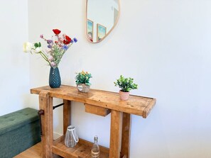 Ein Holzkonsolentisch mit Blumen in einer Vase, zwei Topfpflanzen und einem Spiegel an der Wand.