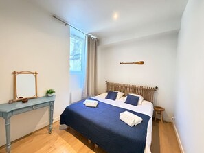 Een slaapkamer met een bed, nachtkastje, spiegel, raam met gordijnen en een houten hoofdbord.