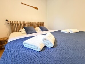 Ein ordentlich bezogenes Bett mit blauer Decke und zwei weißen Handtüchern, ein hölzerner Kopfteil und ein Holzschläger an der Wand.