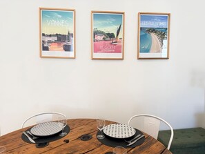 Een eettafel met twee stoelen, een ingelijste poster aan de muur en een glas op de tafel.
