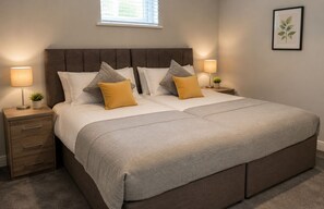 A bedroom with a large bed, two bedside tables with lamps, a small plant, and a framed picture on the wall.