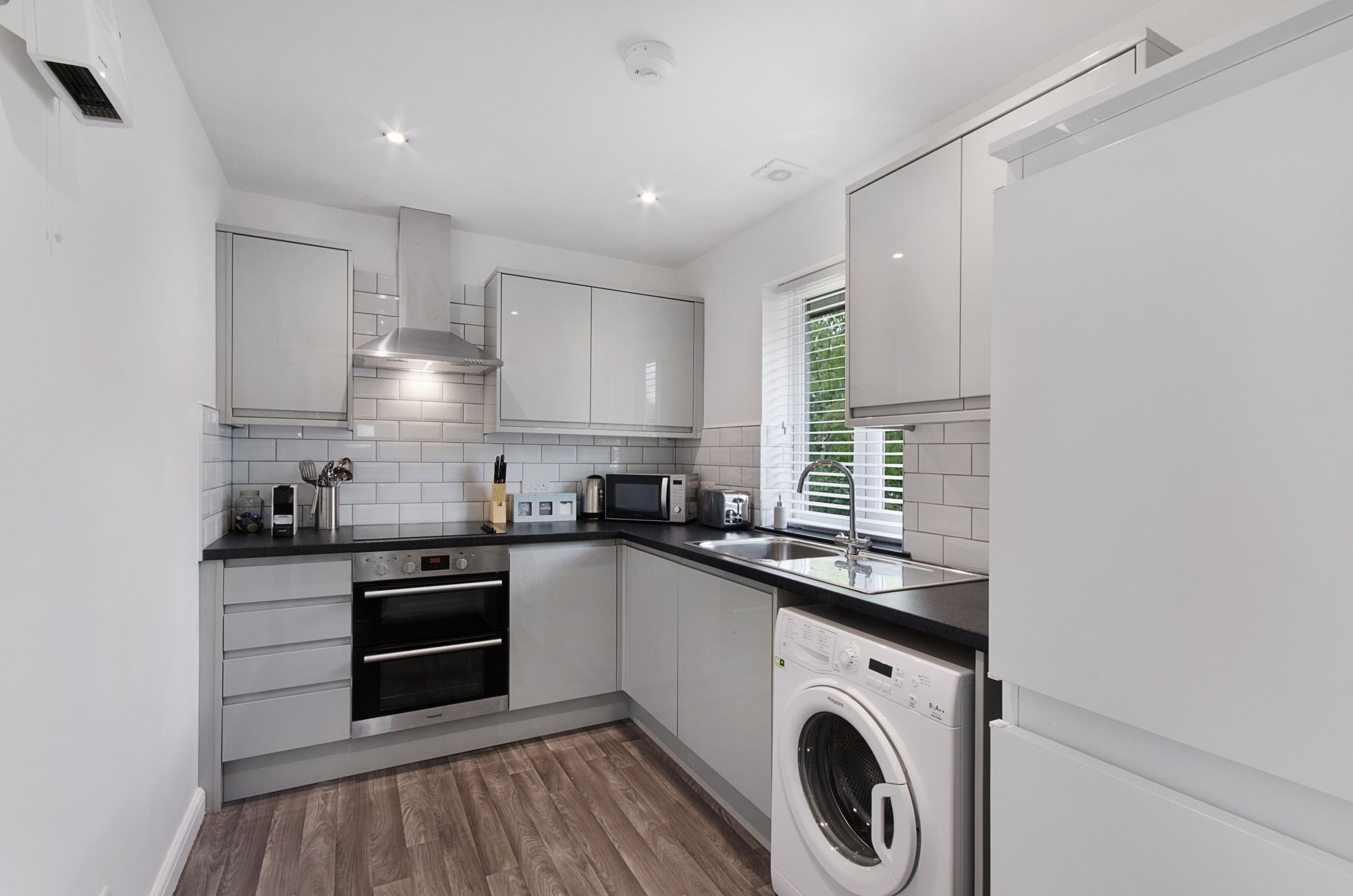 A compact kitchen with white cabinetry, a built-in oven, a microwave, and a washing machine.
