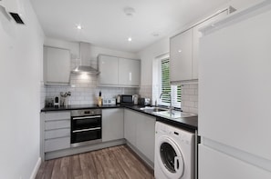 A compact kitchen with white cabinetry, a built-in oven, a microwave, and a washing machine.