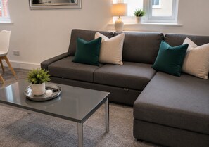 A modern living room with a grey sectional sofa, a small table with a potted plant, and a lamp on a windowsill. - K Suites - The Hatfield Cls (Hatfield)
