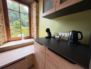 A kitchen with a window, a kettle, a coffee maker, and a bottle of water. - Charming Vacation Rental - Stone and Wood - Morbihan (Saint-Jean-Brévelay)