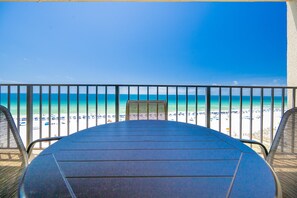 A view from a balcony overlooking a beach with a table and chairs in the foreground. - Phoenix I 1063 2 Bedroom Condo (Orange Beach)