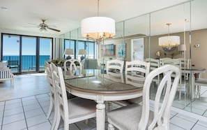 A dining area with a round glass table, white chairs, and a ceiling fan. - Phoenix I 1082 2 Bedroom Condo (Orange Beach)