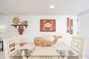 Un coin repas avec une table en verre, des chaises blanches et une décoration centrale repr ésentant une baleine tissée.