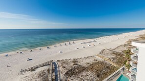 Ein Strand mit Sonnenschirmen, einer Holzpromenade und einem Gebäude mit Schwimmbad.