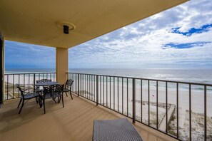 A balcony with a table and chairs, overlooking a beach with a fence and a flag. - Phoenix I 1073 2 Bedroom Condo (Orange Beach)
