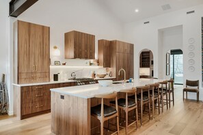 Eine moderne Küche mit Holzschränken, einer zentralen Kochinsel mit Barhocker und einem eingebauten Backofen.