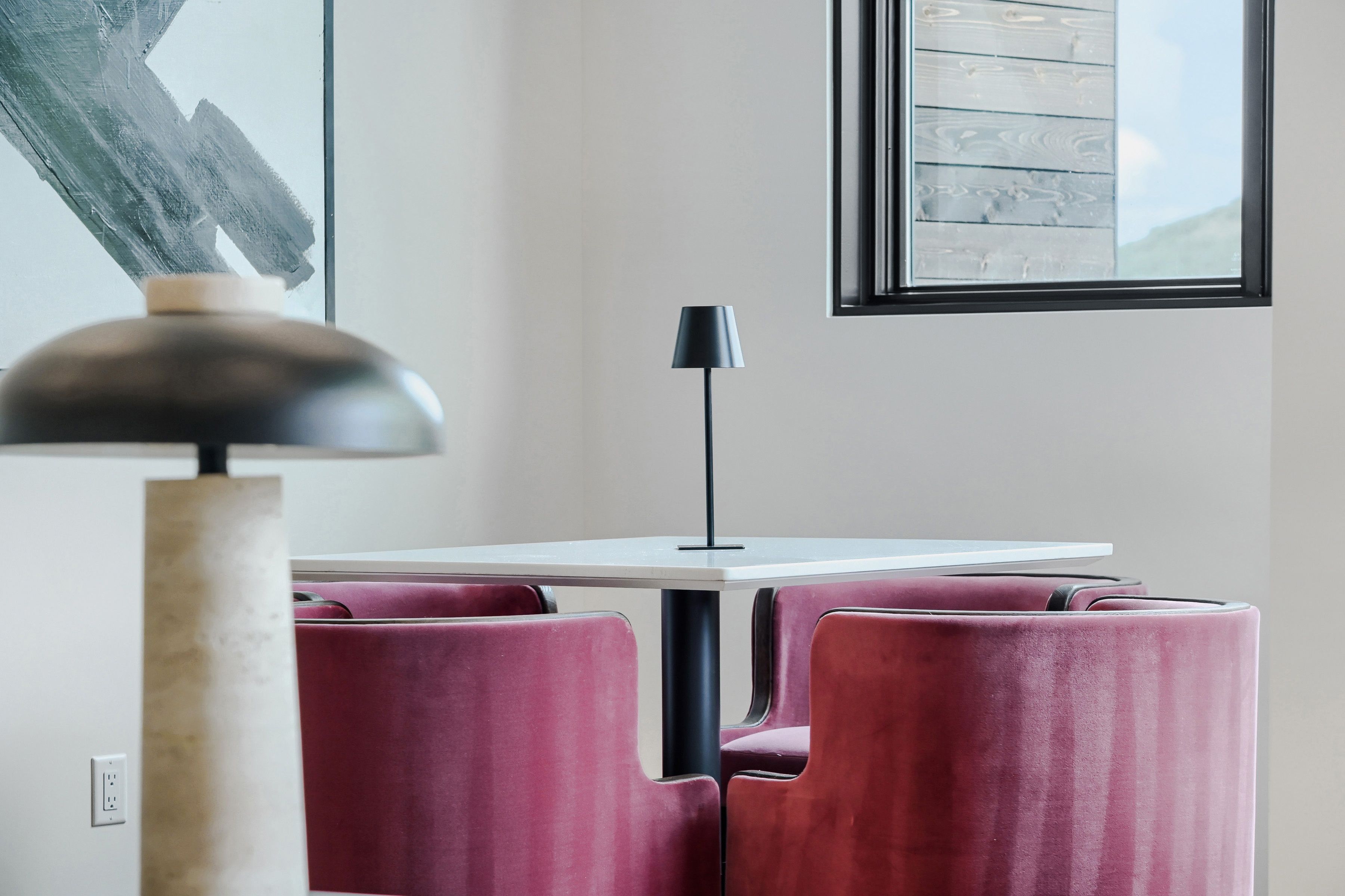 A modern interior with a white table, black lamp, and red upholstered chairs.