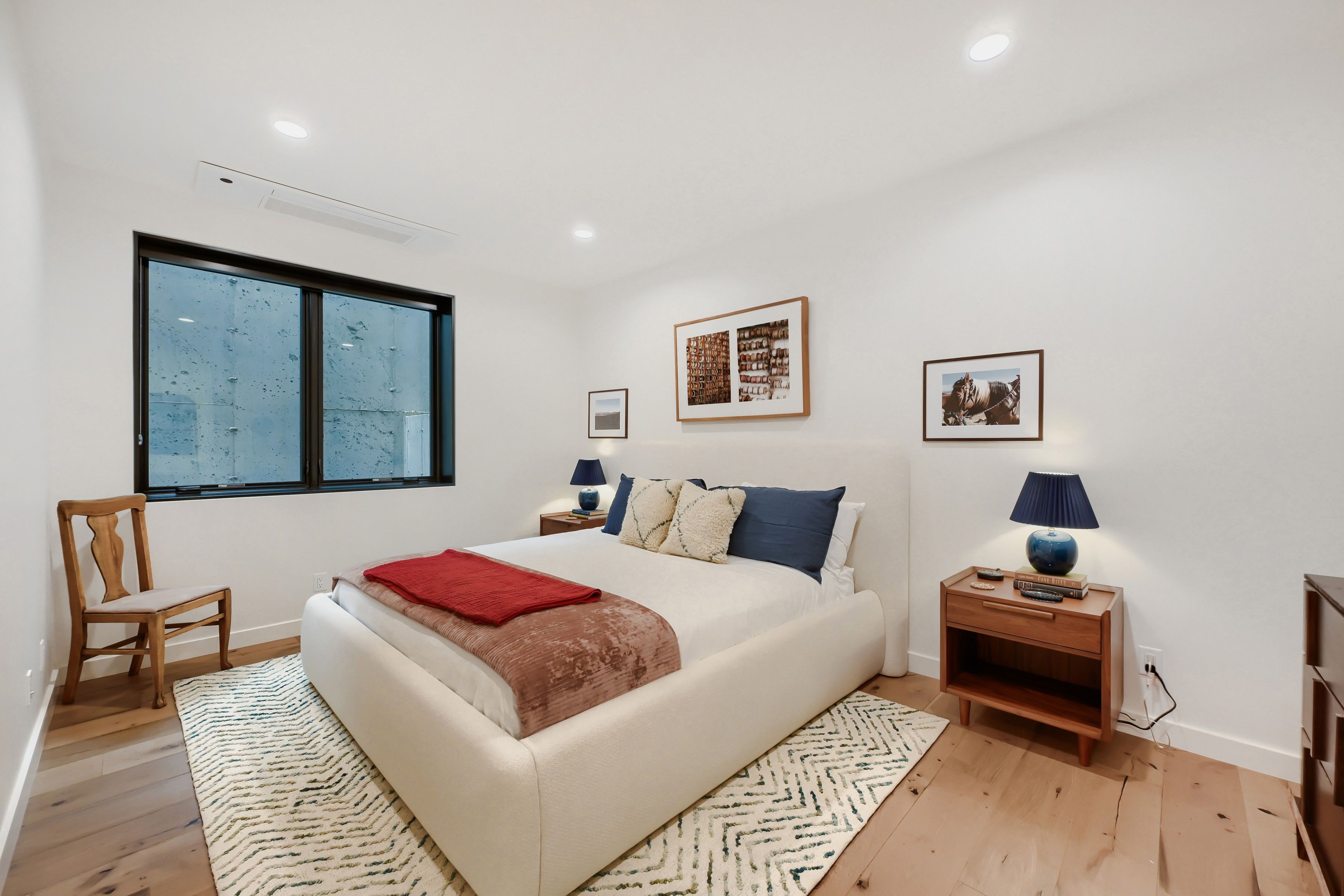 A bedroom with a large bed, a wooden chair, a nightstand with a lamp, and two framed pictures on the wall.