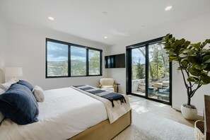 Ein Schlafzimmer mit einem großen Bett, einem an der Wand befestigten Fernseher und Blick ins Freie durch eine Schiebetür.