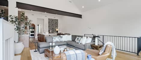 A modern living room with a grey sectional sofa, a coffee table with decorative items, and a view of the kitchen and dining area in the background.