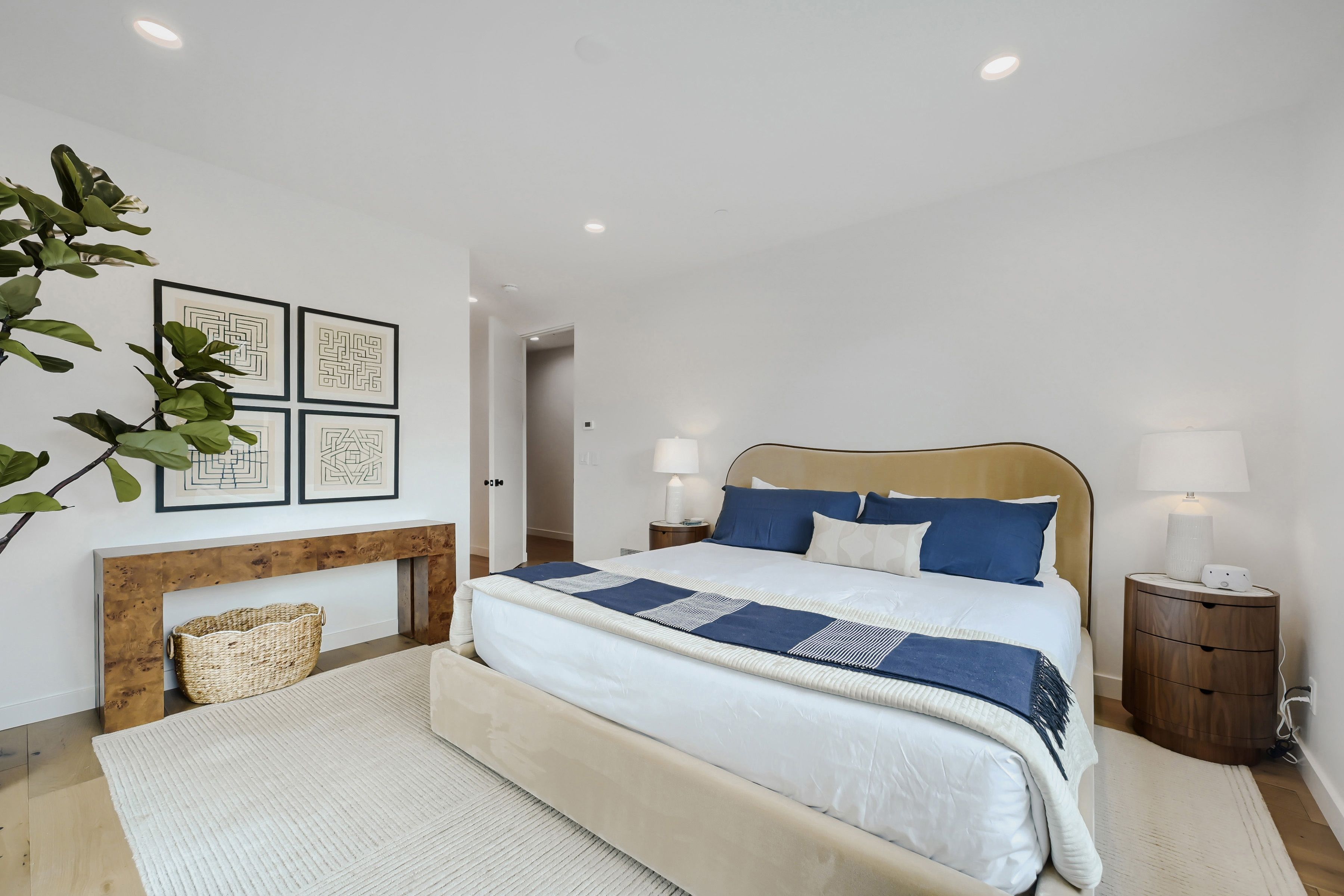 Un dormitorio con cama, mesitas de noche, lámpara y cuadros en la pared.