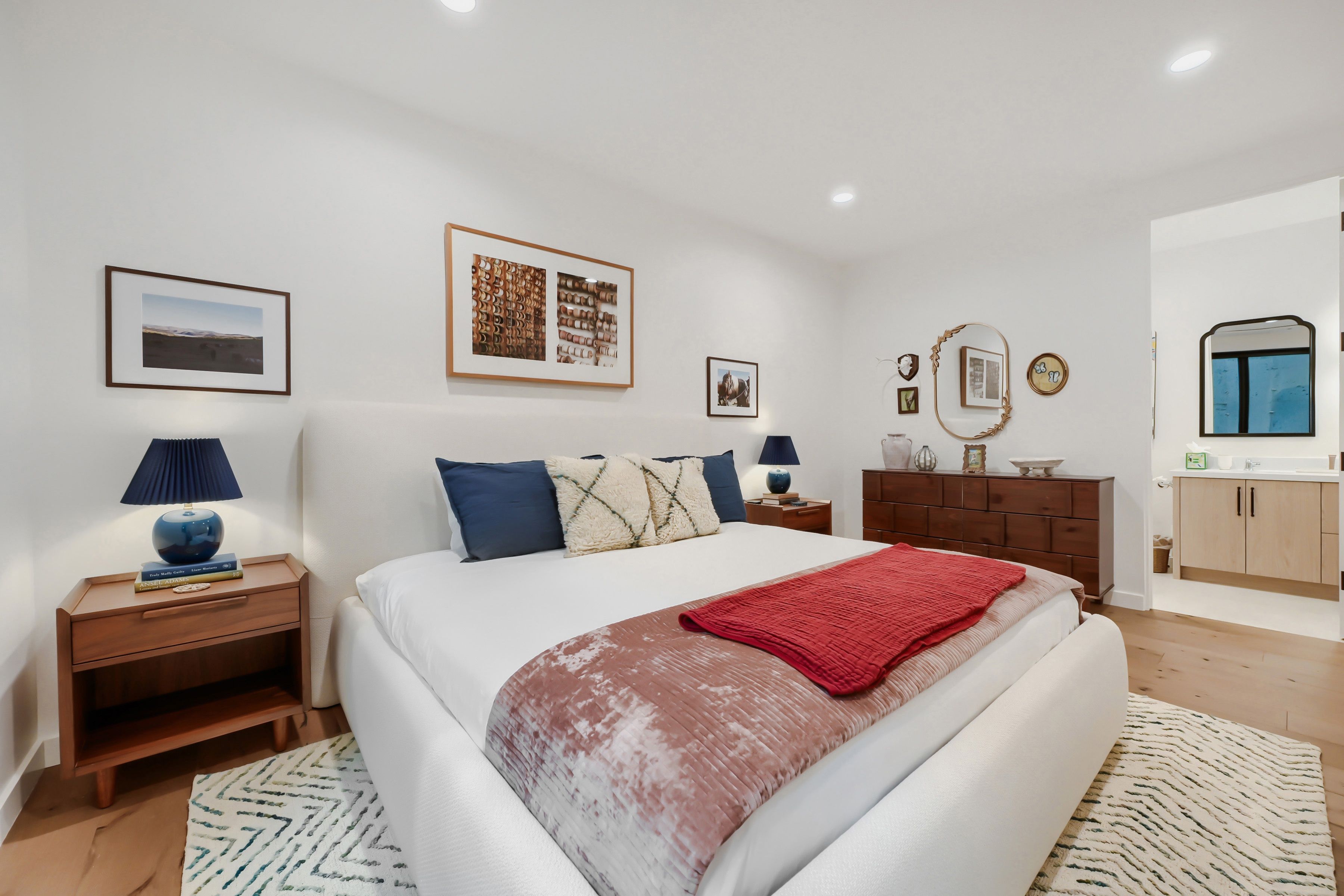 Une chambre à coucher avec un grand lit, deux tables de chevet, une commode, une coiffeuse, un miroir et une fenêtre.