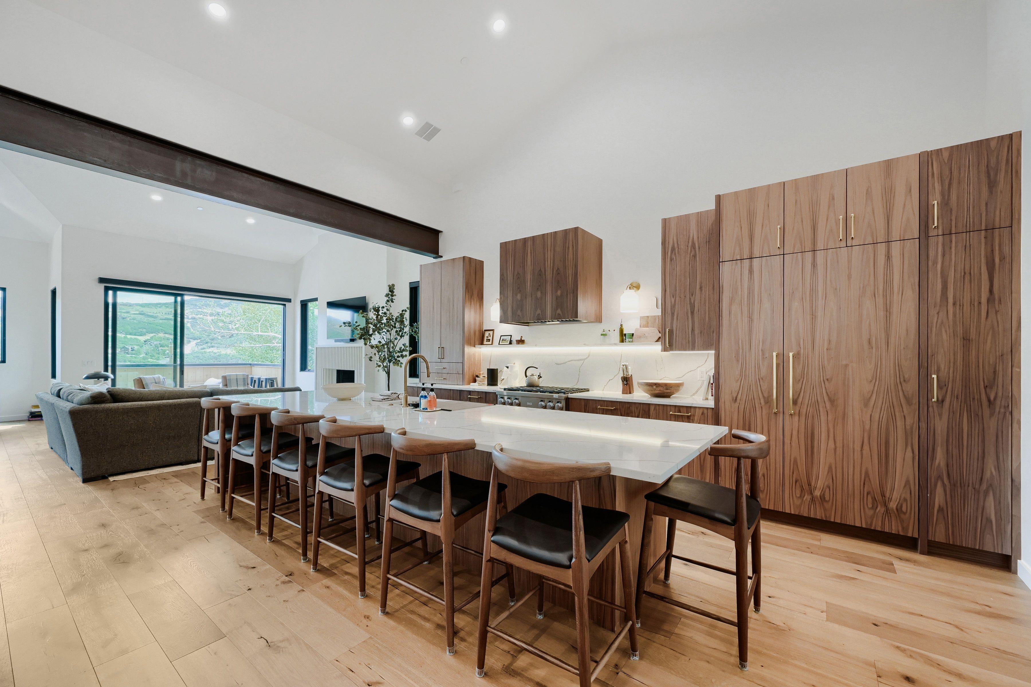 Una cocina moderna con armarios de madera, una isla central con taburetes y un amplio ventanal con vistas a un paisaje verde.