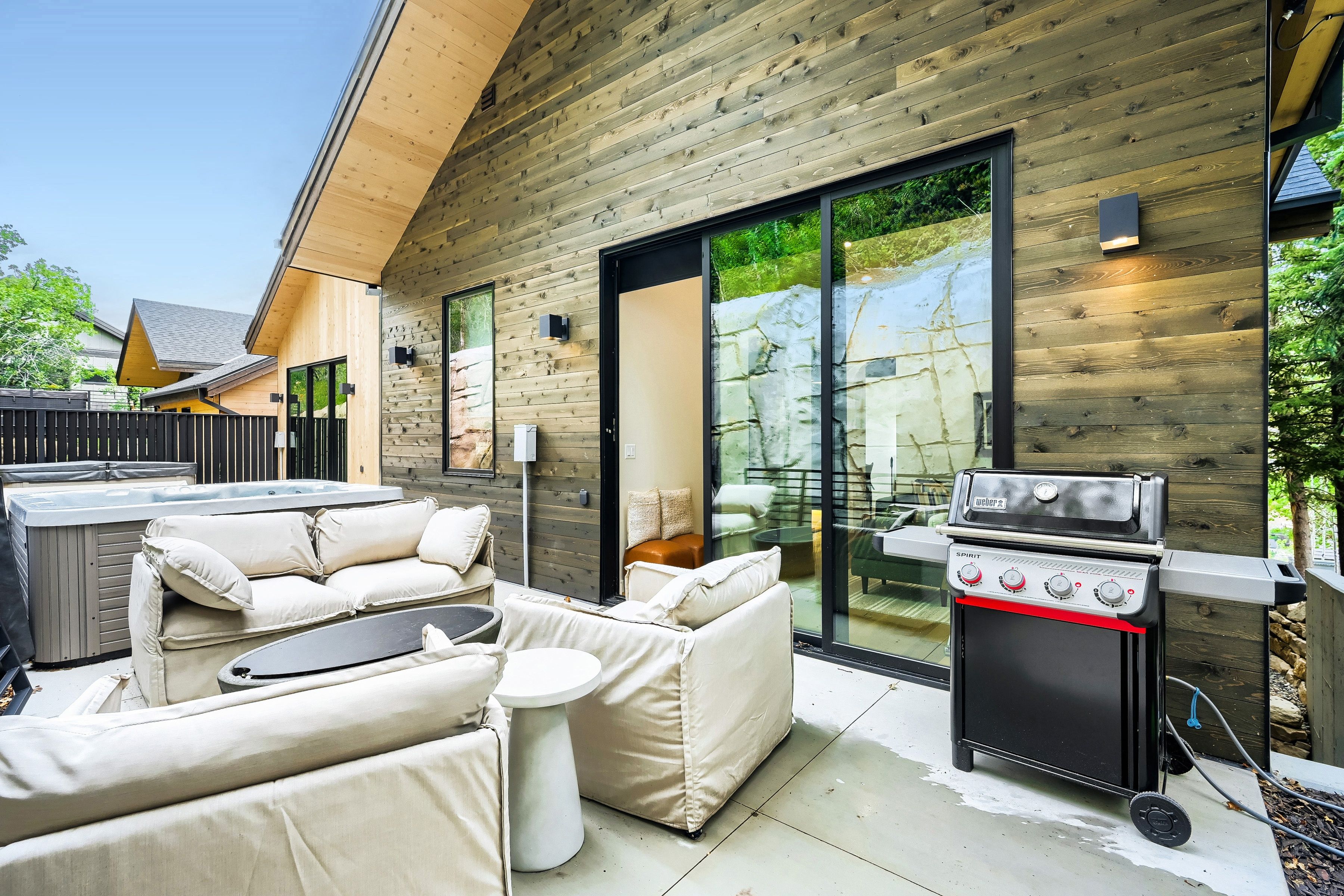 A modern outdoor living space with a wooden deck, a barbecue grill, and a glass sliding door leading to a patio.
