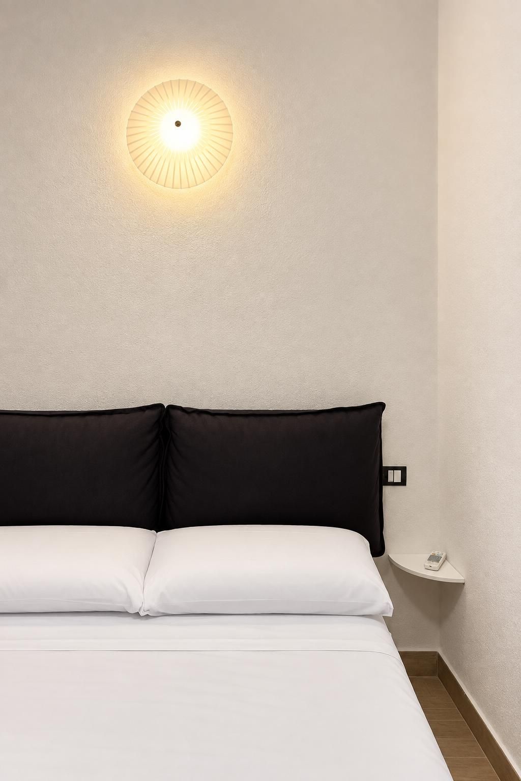 A bed with white bedding, a black headboard, and a wall-mounted light fixture.