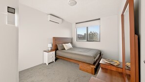 Quarto com cama, mesa de cabeceira, abajur e janela com vista.