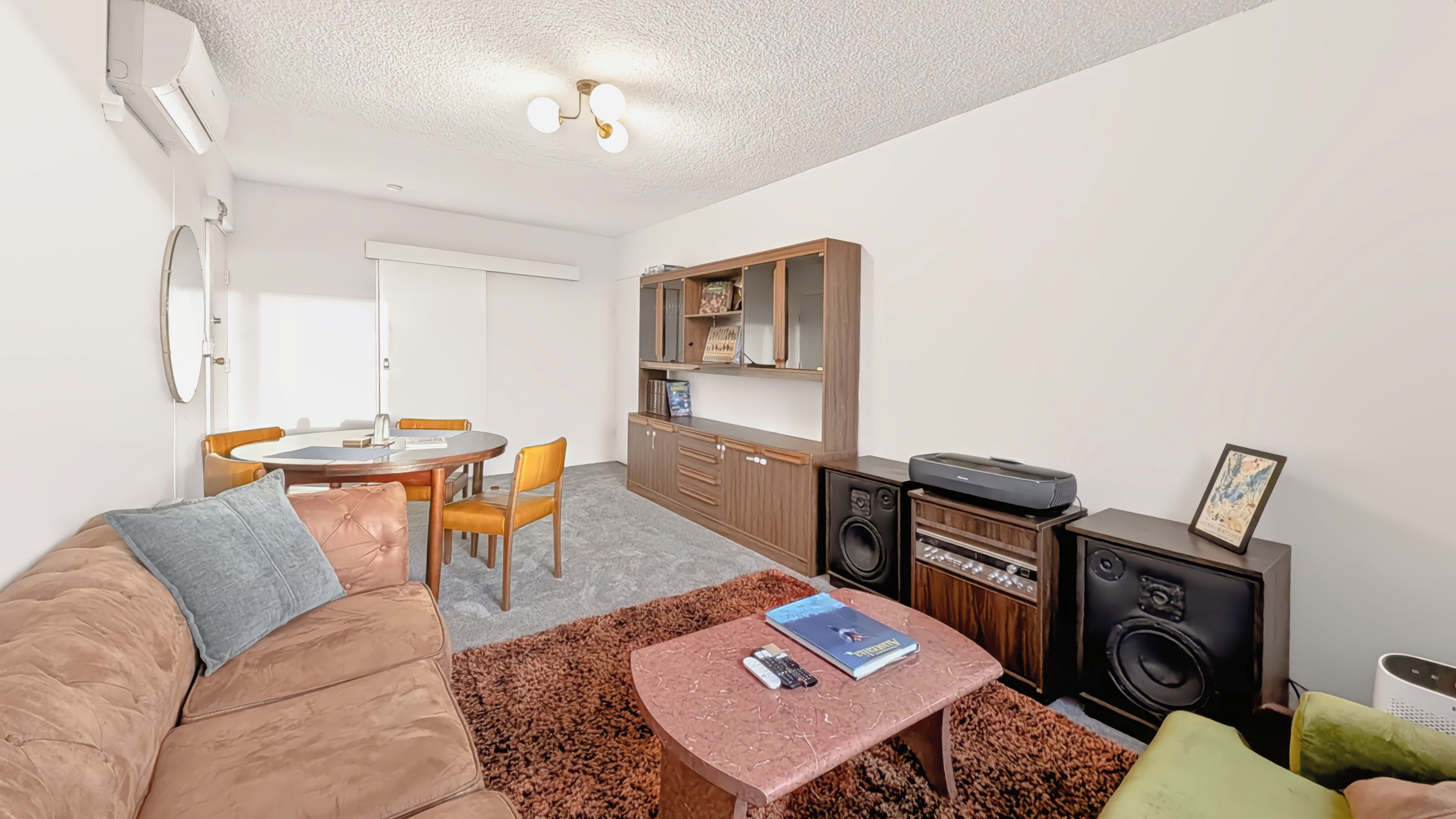 A compact living space with a sofa, a small table, a kitchenette, and a dining area.