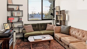 A living room with a green sofa, a brown sofa, a coffee table, and a bookshelf. - 10 mins to Sydney Rd and Lygon St ! Close to the zoo, city, cafes, bar, music ! (Brunswick)