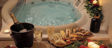 Boblebad omgivet af et udvalg af mad og drikke, herunder en champagneflaske, et glas vin og flere snacks.