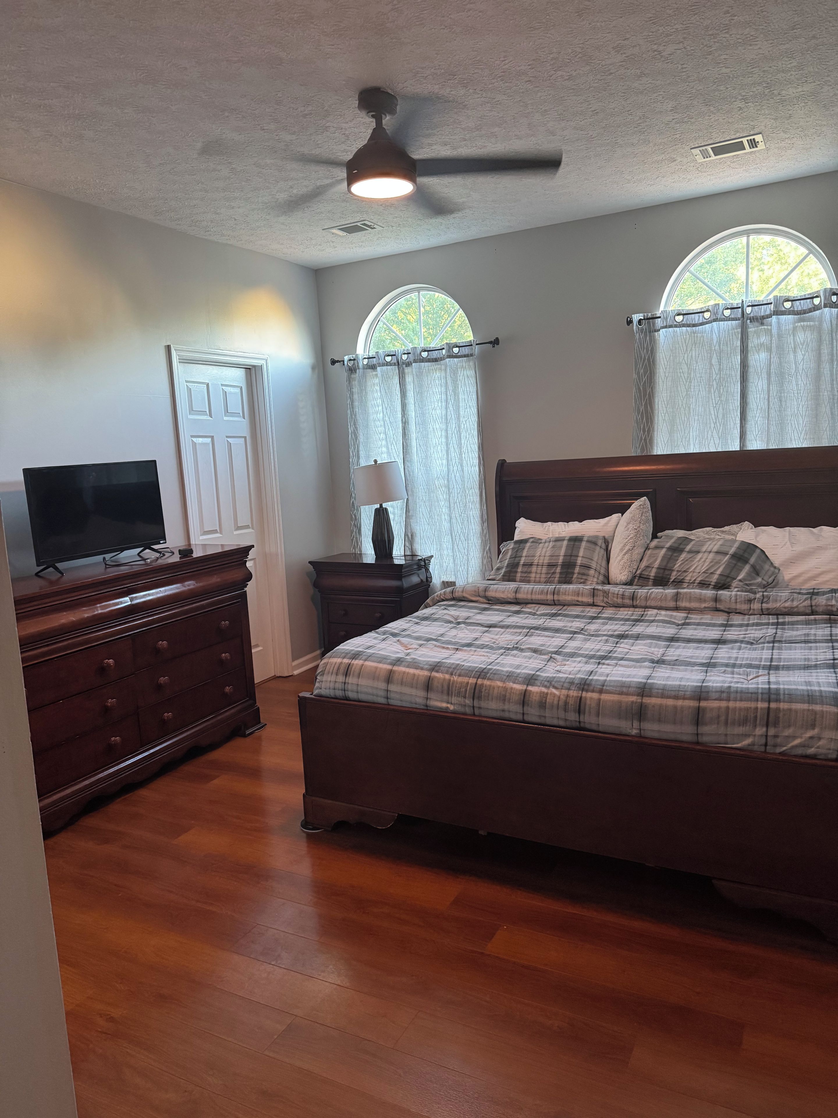 Quarto com cama, cômoda, televisão e ventilador de teto.