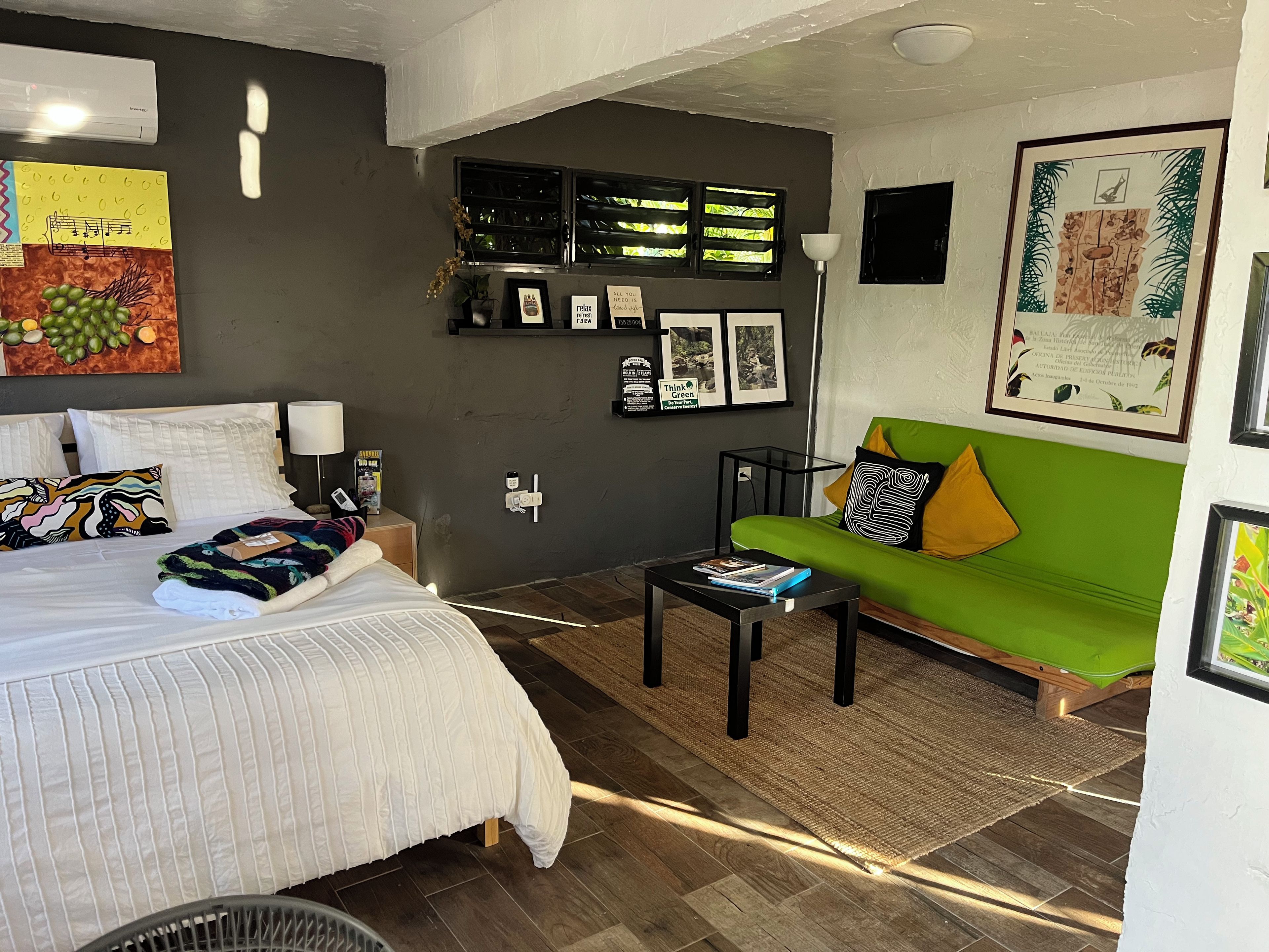 A modern bedroom with a bed, a green sofa, a small table, and a wall with framed pictures and a clock.